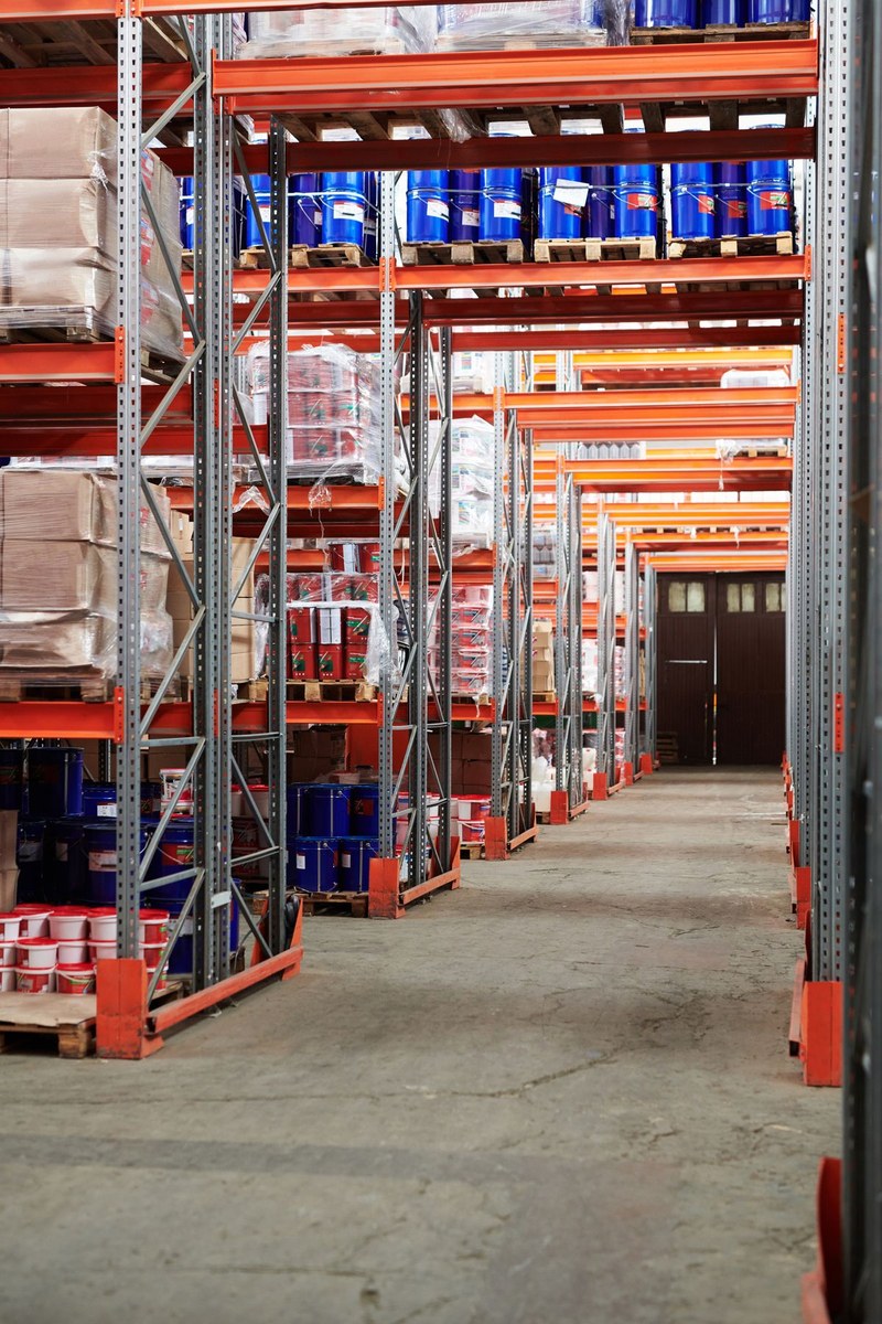 Long warehouse aisle with orange-beam pallet racking packed with pallets